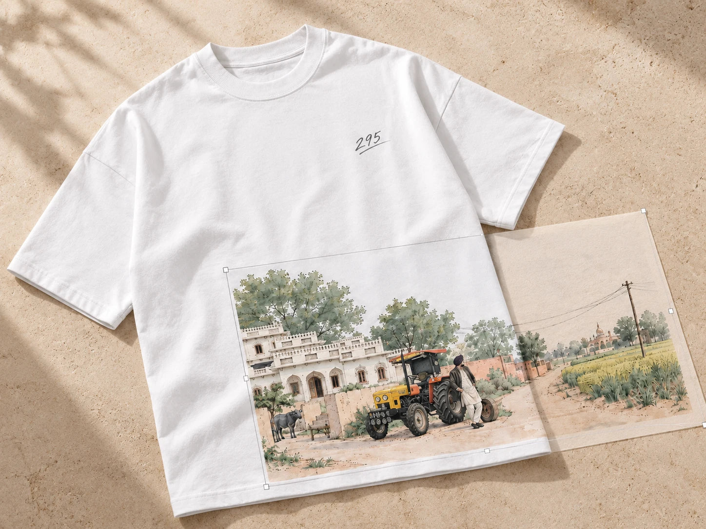 Village artwork being positioned partly on a white tee and partly beside it